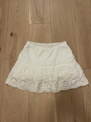 Vit kjol med mönstrad volang - Söt vit kort kjol med bred volangkant och elastisk midja. I kjolen står det 152, men skulle säga att den passar som en xs/s då jag oftast bär s/m och den passar nästan mig fortfarande. 