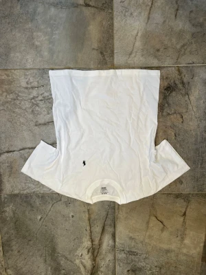 Vit t-shirt från Polo Ralph Lauren - Klassisk vit t-shirt från Polo Ralph Lauren med rund hals och korta ärmar. T-shirten har en liten svart broderad logga på bröstet och är gjord i mjuk bomull för en skön känsla. Perfekt till jeans eller shorts för en clean look.