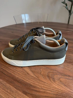 Mörkgröna lädersneakers med vit sula - Stilrena sneakers i mörkgrönt läder med vita gummisulor och mörkgrå skosnören. Skorna har en klassisk låg profil och diskreta sömmar. Insidan är ljusbeige och plösen är grå. Perfekta för en clean och modern look. Storlek 40 men passar även 41