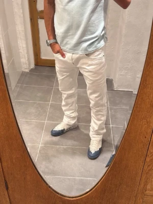 Vita raka jeans med klassisk passform - Säljer ett par vita jeans med rak passform och fem fickor. Jeansen har normal midja och klassisk design med bälteshällor och dragkedjegylf. Perfekta för en clean och fräsch look. Materialet är denim i bomull.