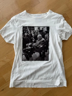 Vit Limitato t-shirt med svartvit fototryck - Vit t-shirt från Limitato med ett stort svartvitt fototryck på framsidan. Klassisk rund halsringning och korta ärmar. Har ett litet hål vid halsen. 