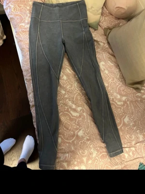 Grå leggings från Lululemon  - Säljer ett par grå leggings med hög midja och dekorativa sömmar längs benen. Materialet är stretchigt och mjukt, perfekt för en bekväm och snygg look. Passar till både oversized tröjor och crop tops. Inga synliga loggor eller märken.