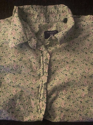 Blommig skjorta från Gant - Säljer en blommig skjorta från Gant i bomull. Skjortan har ett ljust mönster i grönt, rosa och vitt med klassisk krage och knappar framtill. Perfekt för dig som gillar färg och mönster!