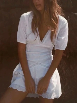 Ny slutsåld student vit klänning  - Söt vit kortklänning med omlott och v-ringning. Klänningen har korta puffärmar och fina spetsdetaljer längs kanterna. Perfekt för varma dagar och har en feminin, luftig känsla. Använd en ända gång 