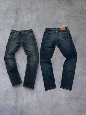 Vintage Levi's jeans (straight fit) - Klassiska blå jeans från Levi's med rak passform och fem fickor. Jeansen har tydliga slitningar och kontrastsömmar, samt den ikoniska läderpatchen bak i midjan. Tillverkade i denim av bomull.