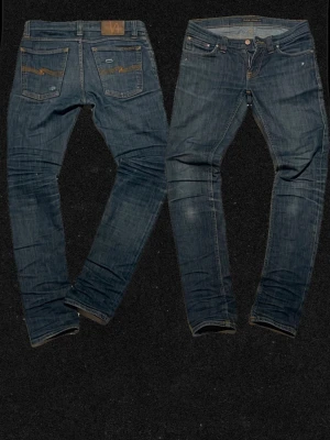 Nudie Jeans Tight Long John 32/32 - Säljer ett par Tight Long John jeans från Nudie Jeans i klassisk blå tvätt med smal passform. Jeansen har orange sömmar, fem fickor och är tillverkade av 98% bomull och 2% elastan för extra stretch. Perfekta för dig som gillar en slimmad look. Inget behöver repareras, Pluss kommer att marknadsföra dem så fort som möjligt när jag har tid. 