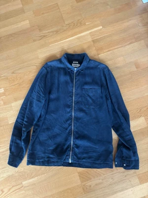 Marinblå linnetröja i zip-modell  East West - Snygg marinblå tröja i zip-modell från  East West i 100% linne. Tröjan har dragkedja framtill, bröstficka och klassisk krage. Perfekt för dig som gillar en avslappnad men stilren look.