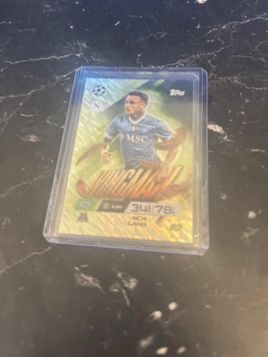 Match Attax Napoli samlarkort - Unik Match Attax samlarkort från Topps med Napoli-tema. Kortet har en färgstark design med spelare i blå Napoli-tröja och texten 'Invincible'. Kortet ligger i ett genomskinligt plastfodral för extra skydd.