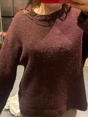 Mörkbrun stickad tröja - Mysig djupvinröd stickad tröja med rund halsringning och långa ärmar. Tröjan har en lätt luddig yta och ribbstickade muddar vid hals, ärmslut och nederkant. Perfekt för kyliga dagar och enkel att matcha med olika outfits. Säljer på grund av brist på användning.