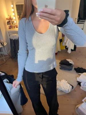 Ljusgrå ribbad långärmad topp - Säljer en ljusgrå ribbad långärmad topp med v-ringning. Toppen har en slim passform och är tillverkad i ett mjukt, stretchigt material som sitter snyggt på kroppen. Perfekt att styla med både jeans och kjol.