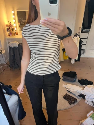 Randig ribbad ärmlös topp - Säljer en vit och svart ribbad topp med smala horisontella ränder. Toppen är ärmlös och har en rak, något lös passform. Perfekt till jeans eller kjol för en enkel och stilren look.