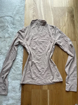 Beige polotopp - Beige polotopp med lång ärm och figurnära passform. Stretchigt och mjukt material. 