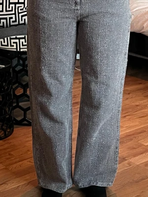 Bruna raka jeans med mönster - Unika grå jeans med vitt rutigt mönster och raka ben. Jeansen har hög midja och bakfickor. Materialet ser ut att vara klassisk denim med en twist tack vare det coola mönstret. Perfekta för dig som vill sticka ut lite extra.