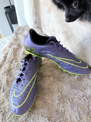  Nike hypervenom fotbollsskor  - Snygga lila fotbollsskor från Nike med stora neongula swoosh-loggor och coola mönster på hälen. Skorna har snörning och en låg profil för bra bollkontroll. Yttermaterialet är syntetiskt och sulan har greppvänliga dobbar för spel på gräs. Dessa är hypervenom Elit och super snygga för dig som vill sticka ut på fotbollsplanen. Priset går att prata om!⚽️🌟