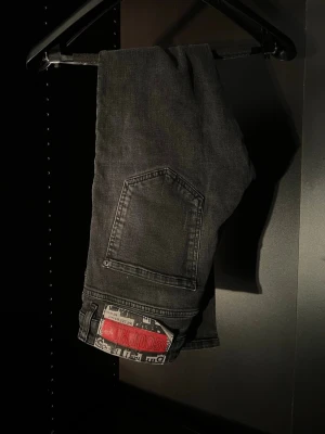 Svarta jeans från Dsquared2 - Säljer ett par svarta jeans från Dsquared2 med raka ben och klassisk femficksdesign. Jeansen har en tydlig röd Dsquared2-logga på bakfickan och är tillverkade i denim. Snygg streetstil och passar perfekt till en trendig outfit.