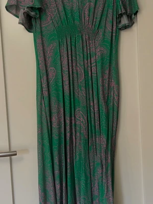 Klänning - Klänning från Culrure, aldrig använd - endast provad. Storlek M. Det är grön botten och rosa paisleymönster. Korta ärmar med lite volang, v-ringad hals och smock i midjan. Lätt och luftig modell, perfekt för varma dagar. Materialet känns mjukt och följsamt.