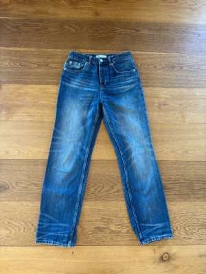 Low waisted Blå raka jeans från ZARA - Säljer ett par klassiska blå jeans från ZARA med rak passform och hög midja. Jeansen har fem fickor, bälteshällor och snygga slitningar för en avslappnad look. Tillverkade i slitstark denim, perfekta till vardagsstilen.