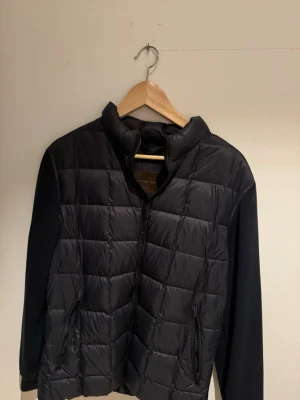 Blå quiltad cardiganjacka - Blå cardiganjacka med quiltat mönster framtill, hög krage och dragkedja. Ärmarna är släta och jackan har två fickor med dragkedja. 