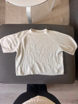Vit stickad topp med korta ärmar - Säljer en vit stickad topp med korta ärmar och rund halsringning. Perfekt för dig som gillar en enkel och clean look. Materialet är mjukt och känns skönt mot huden. Passformen är normal och toppen är lätt att matcha med olika outfits.