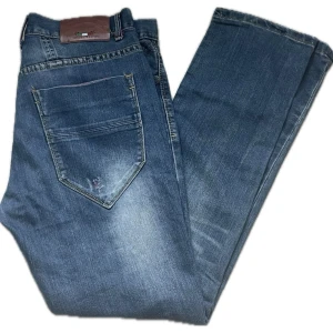 Justing jeans - Snygga blå jeans från Justing Jeans med raka ben och klassisk femficksmodell. Jeansen har en läderpatch bak i midjan och slitna detaljer på bakfickan. Tillverkade i denim med kontrastsömmar och normalhög midja.