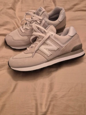 Beige New Balance sneakers - Snygga beige sneakers från New Balance med klassisk design och stora vita N-loggor på sidorna. Skorna har ovandel i mesh och mocka, vita snören och en bekväm sula med svart yttersula. Perfekta för dig som gillar stilrena och sportiga sneakers. Helt nya 