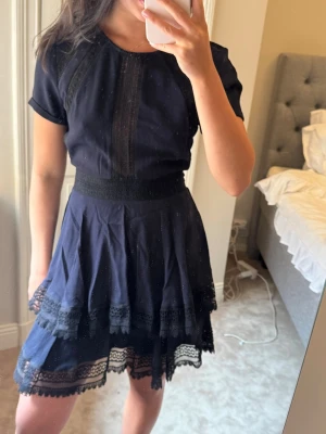 Maje klänning. Marinblå kort klänning med spetsdetaljer.  - Supersöt marinblå maje kortklänning med spetsdetaljer och volanger. Klänningen har rund hals, korta ärmar och markerad midja. 