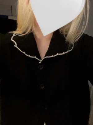 Svart kofta med vita detaljer  - Stilren svart kofta med dekorativ vit kant runt kragen och ärmarna🤍Materialet är mjukt och bekvämt. Storlek XL men skulle säga att den passar S/M. Köpt secondhand men har själv aldrig använt✌️