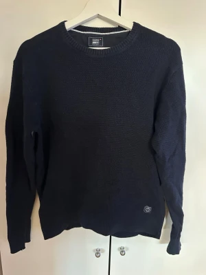 Mörkblå stickad tröja från Signal - Klassisk mörkblå stickad tröja från Signal med rund halsringning och diskret logomärke nertill. Tröjan har lång ärm och ribbade muddar vid ärmslut och nederkant. Perfekt för lager på lager och enkel att matcha med olika stilar.