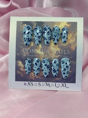 SkyClaw (XS);Medium Almond - Handgjorda press-on naglar i storlek XS: 14 mm, 11 mm, 11,5 mm, 10 mm, 8 mm. Naglarna har en ljusblå bas med handmålade mörkblåa leopardmönster och en glansig finish. Formen är medium långa almond. Perfekt för dig som vill ha en unik och trendig look.