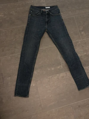 Tiger or sweden jeans - Säljer ett par mörkblå jeans från tiger of sweden med smal passform och klassisk femficksdesign. Jeansen har en snygg tvätt och raka ben. Tillverkade i slitstarkt denimtyg med detaljerade sömmar och metallknappar. 