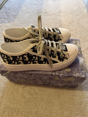 Dior Oblique sneakers i canvas - Snygga låga sneakers från Dior med klassiskt blått och vitt Oblique-mönster på canvas. Skorna har vita gummisulor med svart stjärndetalj undertill och vita snören. Märkeslogga på plösen och sidan. Perfekta för dig som vill ha en lyxig och trendig look.