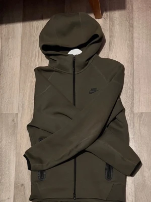 Olivgrön Nike hoodie med dragkedja - Säljer denna olivgröna nike tech hoodie i storlek S. Använt fåtal gånger så inga problem på den. Set med byxor kan också köpas för 1300.