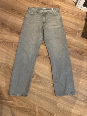 Grå raka jeans från Jack & jones  - Säljer ett par grå jeans från Jack & jones med rak passform och klassisk femficksdesign. Jeansen är tillverkade i denim och har en enkel, stilren look som passar till det mesta. Perfekta för dig som gillar en avslappnad och trendig stil.