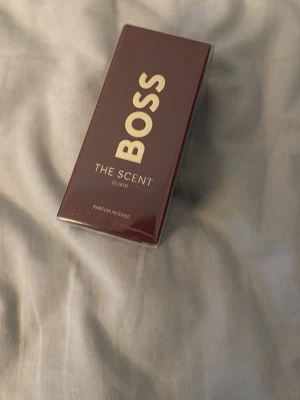 BOSS The Scent Elixir Parfum Intense - BOSS The Scent Elixir Parfum Intense kommer i en elegant, mörkröd rektangulär kartong med guldiga detaljer. Förpackningen är tillverkad av kartong och har en lyxig känsla. Perfekt för dig som gillar exklusiva dofter och snygg design.
