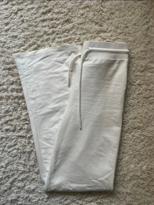 Low waist fitted pants - Säljer ett par vita mjukisbyxor med resår i midjan och dragsko för skön passform. Byxorna har raka ben och är gjorda i ett mjukt och bekvämt material, perfekta för chill dagar hemma eller när du vill vara extra comfy.