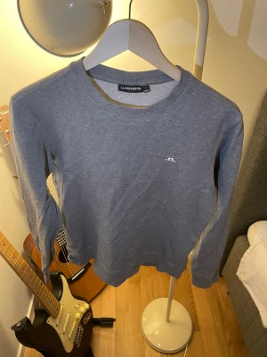 Grå sweatshirt från J.Lindeberg - En stilren grå sweatshirt från J.Lindeberg med rund halsringning och diskret logga broderad på bröstet. Tröjan har långa ärmar och är tillverkad i mjukt bomullsmaterial. Perfekt för en avslappnad och trendig look.