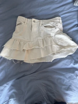 Vit volangkjol från Perfect Jeans - Supersöt vit kortkjol från Perfect Jeans med dubbla volanger och råa kanter. Kjolen har klassisk jeanslook med fickor fram och bak samt knapp och dragkedja. Perfekt för dig som vill ha en trendig och lekfull stil.