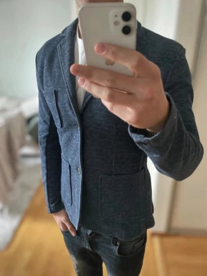 Blå kavaj Selected Homme - Snygg mörkblå kavaj med två stora patchfickor framtill och klassisk krage. Kavajen har två knappar och är tillverkad i ett mjukt, stickat material som ger en avslappnad men stilren look. Perfekt för dig som vill ha en modern twist på klassikern.