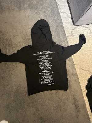 Svart Kendrick Lamar hoodie - Säljer en svart hoodie med tryck från Kendrick Lamars 'Mr. Morale & The Big Steppers'. Stor vit text på ryggen med låttitlar och mindre tryck framtill. Klassisk passform med huva och dragsko. Perfekt för dig som gillar streetwear och musikmerch.