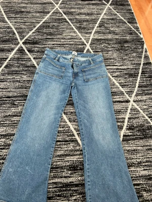 Blå utsvängda jeans med fickor - Snygga blå jeans med utsvängda ben och stora framfickor. Klassisk femficksmodell baktill och dubbla knappar i midjan. Perfekta för dig som gillar retrostil och vill ha ett par jeans med lite extra attityd.