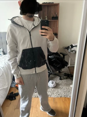 Vit hoodie med svart ficka och huva - Säljer en vit hoodie från Sail racing med svart huva och stor svart magficka. Dragkedja framtill och patch med logga på vänster ärm. Perfekt för dig som gillar streetwear och vill ha något stilrent men ändå unikt.