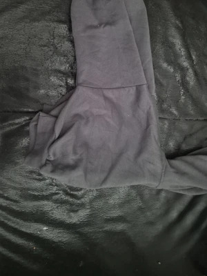 Svart hoodie med huva - En enkel svart hoodie med klassisk huva och ribbade muddar vid ärmsluten. Hoodien har en avslappnad passform och är tillverkad i mjukt bomullsmaterial, perfekt för en chill och stilren look.