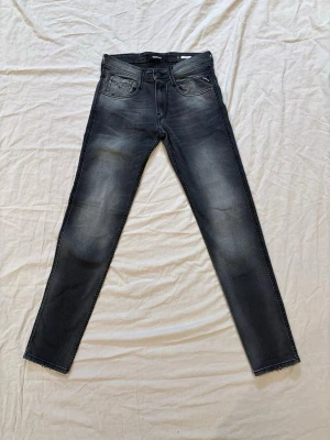 Svarta slim fit jeans från Replay - Säljer ett par svarta slim fit jeans från Replay med snygg faded effekt och klassiska fem fickor. Jeansen har raka ben och detaljerade bakfickor med broderi. Materialet är stretchigt denim som ger en bekväm passform.
