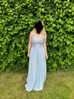 ljusblå balklänning/långklänning med spetsdetaljer - Elegant ljusblå långklänning med spetsdetaljer och djup v-ringning. Klänningen har en luftig passform och är perfekt för sommarens festligheter. Den har tunna axelband och en vacker fallande kjol. 