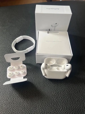 Apple AirPods Pro trådlösa hörlurar - Säljer ett par vita Apple AirPods Pro med laddningsetui, extra silikonpluggar och laddningskabel. Hörlurarna har en stilren och kompakt design i blankt plastmaterial och levereras i originalförpackning. Perfekta för musik, samtal och träning.