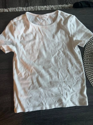 Vit ribbad t-shirt - En basic vit ribbad t-shirt med rund halsringning och korta ärmar. Perfekt att matcha med jeans eller kjol för en clean och enkel look. Tillverkad i mjuk bomull som känns skön mot huden.