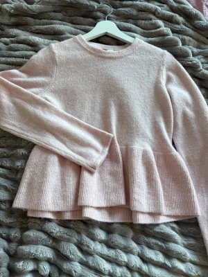 Ljusrosa stickad volangtröja - Supersöt ljusrosa stickad tröja med volang nertill och rund hals. Tröjan har långa ärmar och är gjord i ett mjukt, fluffigt material som känns riktigt mysigt. Perfekt för dig som gillar en feminin och trendig look. Storlek M men sitter mer som en S. Aldrig använd