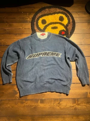 Blå stickad Supreme tröja - Supersnygg blå stickad tröja från Supreme med stort vitt Supreme-tryck över bröstet. Tröjan har rund halsringning, ribbade muddar vid ärmslut och nederkant.
