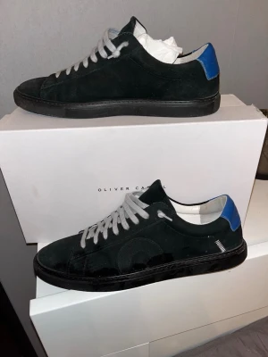 Oliver cabell sneakers - Säljer ett par svarta Oliver Cabell low sneakers med blå häl. Använda endast några gånger, mycket fint skick. Säljer pga att skorna ej kommer till användning. Perfekta vardagssneakers – minimalistiska och stilrena👌🏻