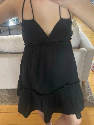 Svart kort klänning med tunna band - Söt svart kort klänning med tunna axelband och v-ringning. Klänningen har volangdetalj nedtill och en luftig passform. Storlek xxs men luftig och ”stor” i storlek så mer som xs/s